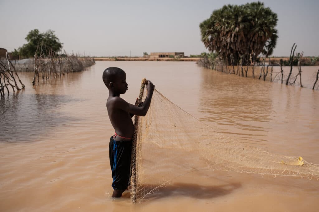 A boy puts up a net to catch fish in the flood waters covering a road outside his home in Odobere on October 21, 2024. - Floods along the Senegal river have affected over 55,000 people after heavy rain in the Senegal River Basin leaving many villages underwater and over 1,000 hectares of farm land submerged. (Photo by GUY PETERSON / AFP)