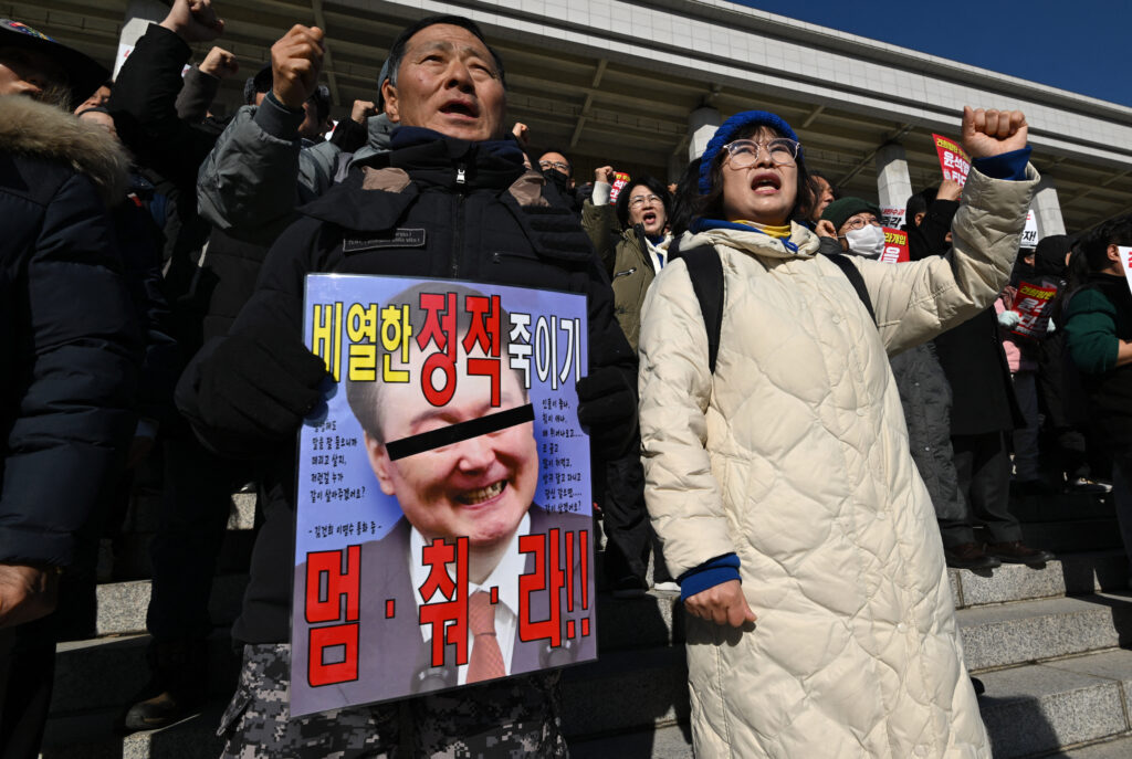 Members of South Korea's main opposition Democratic Party hold a placard showing a damaged picture of South Korean President Yoon Suk Yeol during a rally against him at the National Assembly in Seoul on December 4, 2024, after South Korea President Yoon lifted martial law just hours after he imposed it. | Photo by JUNG YEON-JE / AFP