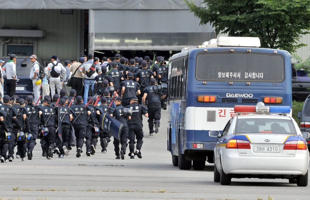 ‘Squid Game’: Real-life violence that inspired South Korean show. (FILES) Riot police walk into a building still held by striking workers as a police bus to escort the strikers is seen at Ssangyong Motor in Pyeongtaek, some 70 kms south of Seoul, on August 6, 2009. The car plant turned into a battlefield pitting riot police armed with tasers and an activist who spent 100 days perched atop a tower. This labor unrest that inspired Netflix's most successful show ever. (Photo by JUNG YEON-JE / AFP)