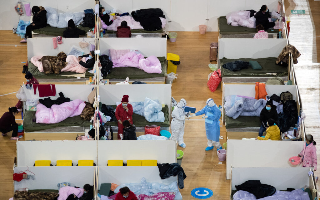 (FILES) This photo taken on February 18, 2020 shows medical personnel walking among patients with mild symptoms of the COVID-19 coronavirus resting at night in the temporary Hospital set up in a sports stadium in Wuhan, in China's central Hubei province. Photo by AFP [FILE PHOTO]