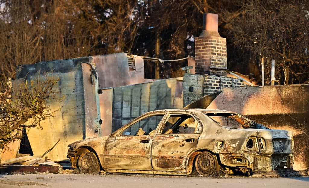 LA wildfire victims include man holding a hose, dad at his son’s bedside. A fire-ravaged vehicle sits in the driveway of a burnt down home in Altadena, California on January 10, 2025, as a 6pm to 6am curfew went into effect following the Eaton fire, to prevent looting. | Photo by Frederic J. BROWN / AFP