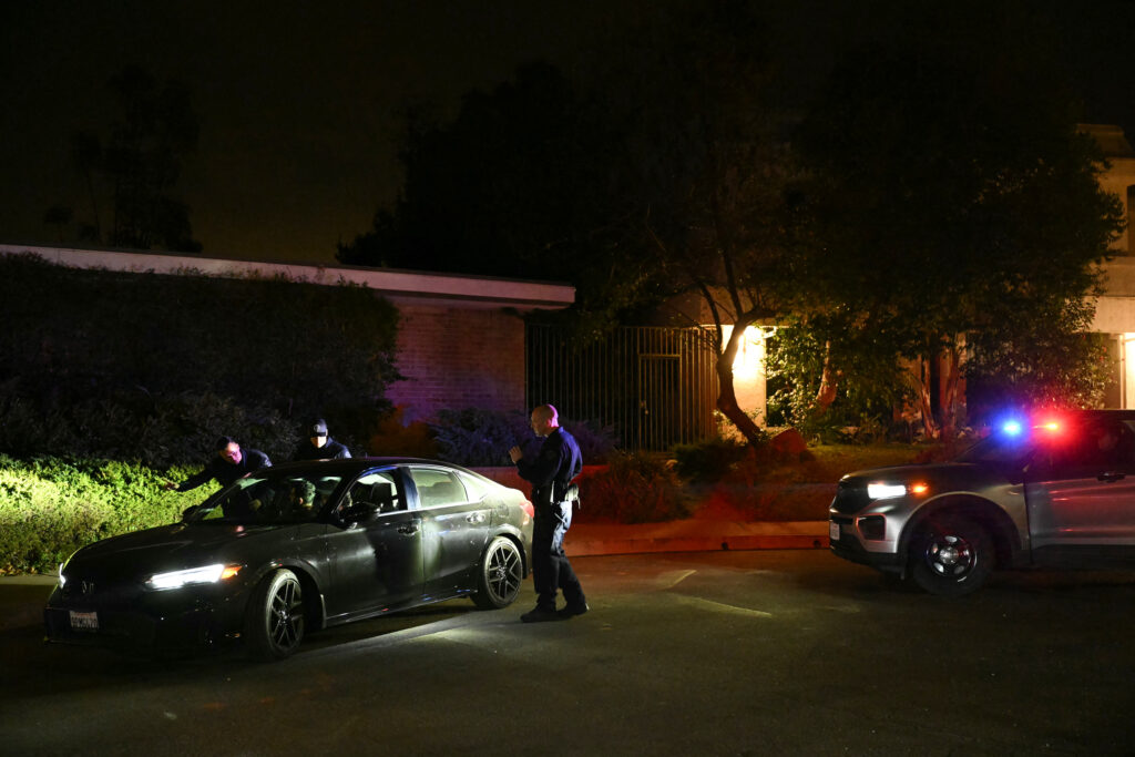 LAPD officers investigate a vehicle while enforcing a new evacuation order as smoke and flames from the Palisades Fire burn towards Encino and Tarzana neighborhoods, in Los Angeles, California, January 10, 2025.| Photo by Patrick T. Fallon / AFP