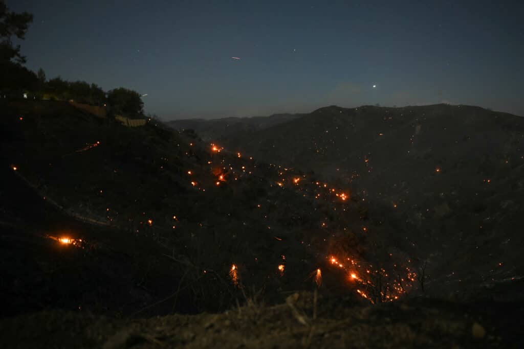 A hillside smolders as the Palisades fire grows near the Mandeville Canyon neighborhood and Encino, California, on January 11, 2025. The Palisades Fire, the largest of the Los Angeles fires, spread toward previously untouched neighborhoods January 11, forcing new evacuations and dimming hopes that the disaster was coming under control. | Photo by Patrick T. Fallon / AFP