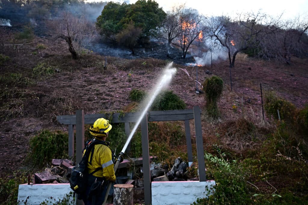 A firefighter puts out flames in the Mandeville Canyon neighborhood of Los Angeles, California, on January 11, 2025, as the Palisades Fire continues to burn.| Photo by AGUSTIN PAULLIER / AFP