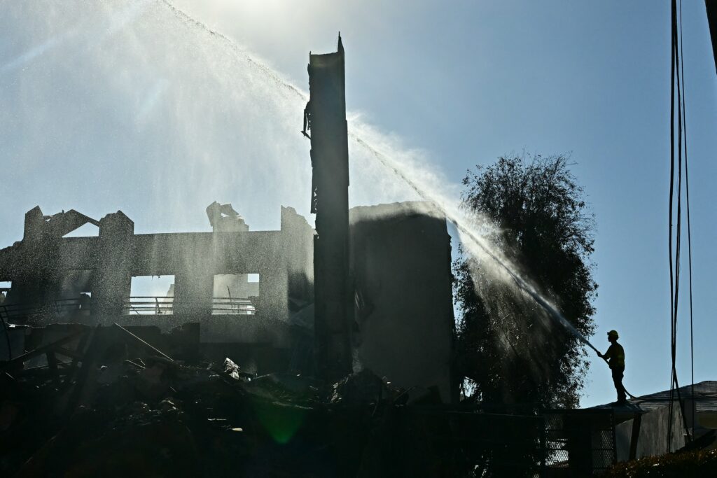 A firefighter douses a structure burned by the Palisades Fire in the Pacific Palisades neighborhood of Los Angeles, California, on January 12, 2025. | Photo by Frederic J. Brown / AFP