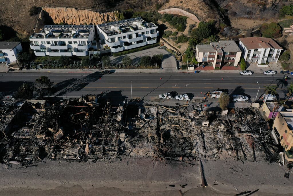 An aerial image shows utility crews working behind homes destroyed by the Palisades Fire along the Pacific Coast Highway in Malibu, California, on January 15, 2025. | Photo by Patrick T. Fallon / AFP