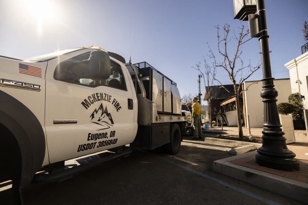 A private firefighting company employee, hired to protect Rick Caruso's Palisades Village mall from the Palisades Fire, stands near a vehicle at the mall in Pacific Palisades, California, on January 15, 2025. |Photo by ETIENNE LAURENT / AFP