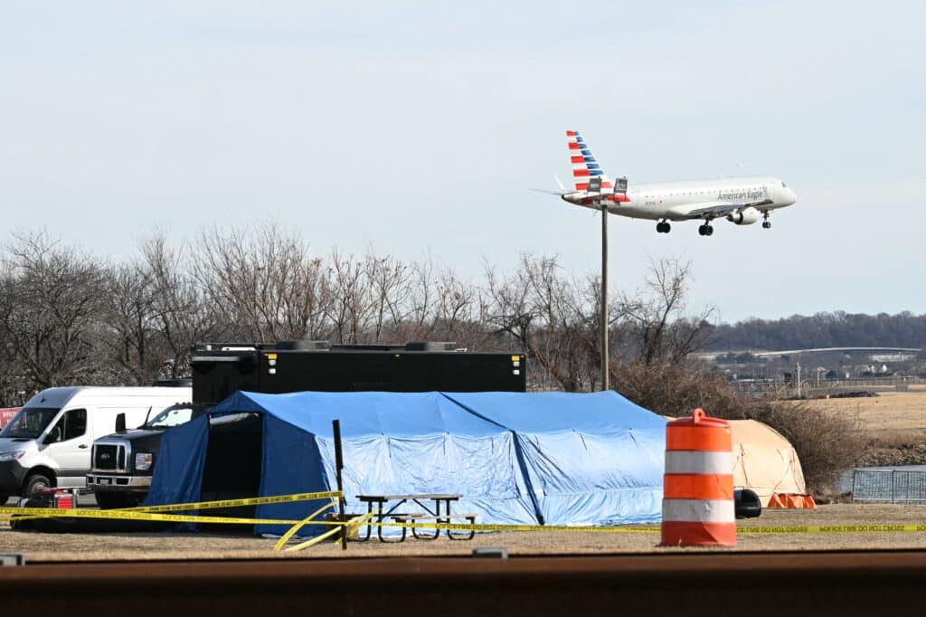 An American Eagle plane lands at Reagan National Airport as investigators use a temporary shed to gather pieces of wreckage after American Airlines flight 5342 on approach to the airport collided with a US Army helicopter, near Washington, DC, on January 30, 2025. | Photo by ANDREW CABALLERO-REYNOLDS / AFP