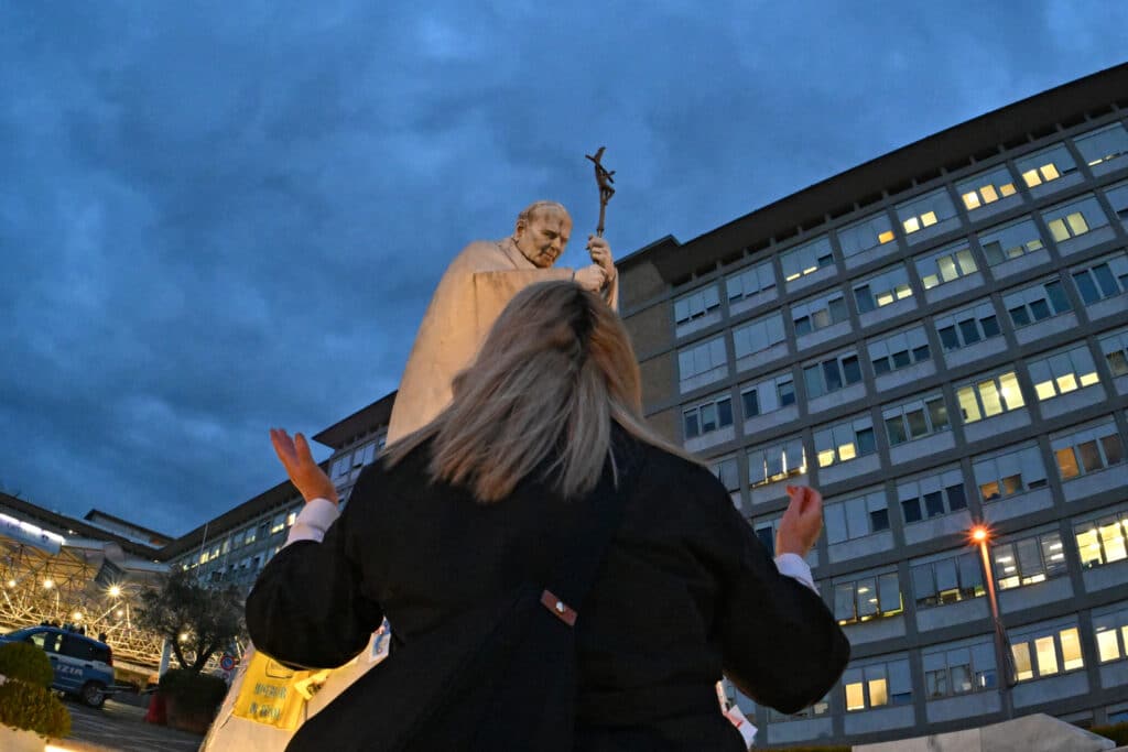 A woman prays at the statue of John Paul II outside the Gemelli University Hospital where Pope Francis is hospitalized with pneumonia, in Rome on March 9, 2025 (Photo by ANDREAS SOLARO / AFP or licensor / AFP)